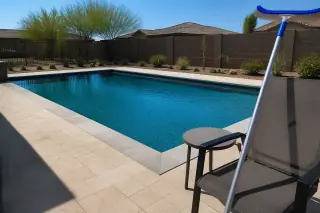 Crystal clear rectangular swimming pool with desert landscaping and a pool brush on a patio chair in Phoenix, AZ.