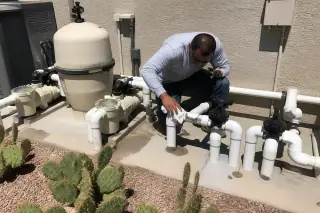 Technician cleaning around pool pumps and new PVC plumbing on a concrete slab in a Phoenix, AZ backyard.