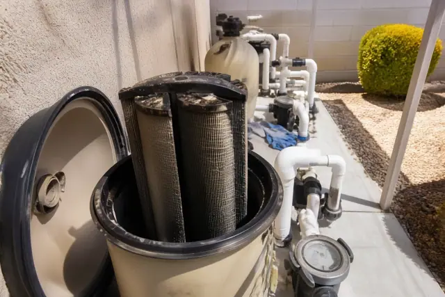 A pool technician cleaning debris-filled filter cartridges on a pool equipment pad in Glendale, AZ.