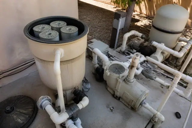 A technician cleaning pool filter cartridges on a concrete equipment pad in Phoenix, AZ.