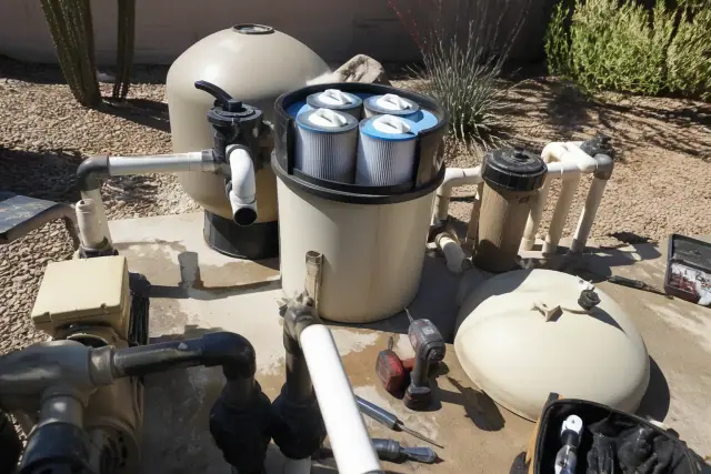 Open pool filter housing with internal cartridges and maintenance tools on a concrete equipment pad in Mesa, AZ.