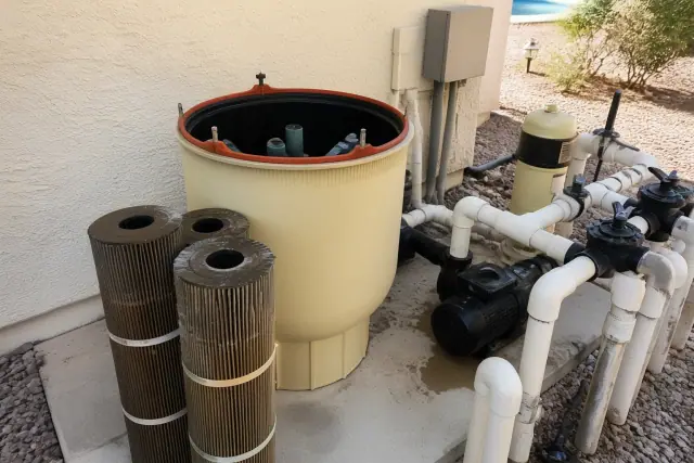 A technician cleaning pool filter cartridges on a concrete slab at a residential property in Phoenix, AZ.