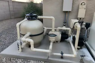 Cleaned pool filter housing and wiped-down piping on a concrete equipment slab in a Phoenix, AZ backyard.