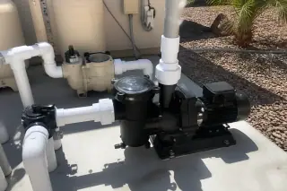 Repaired pool pump with new PVC couplings and bolts on a concrete slab in a Phoenix, AZ backyard.