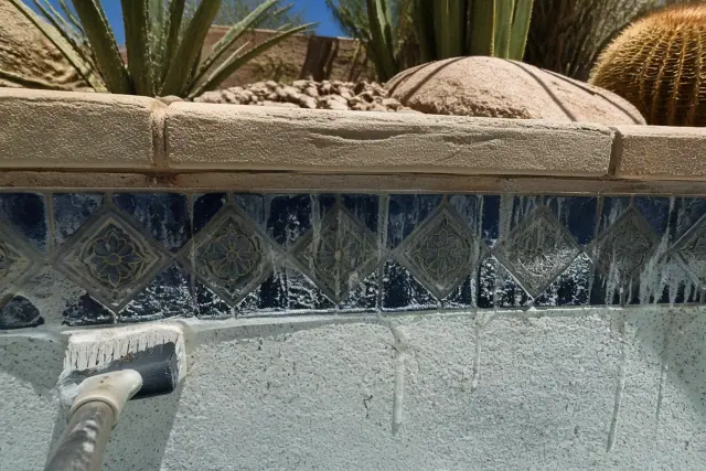 Close-up of mineral deposits being cleaned from pool waterline tiles in Phoenix, AZ, with desert landscaping in the back.