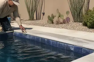 Contractor cleaning pool waterline tiles by a rectangular backyard pool in Phoenix, AZ.