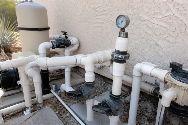Pool plumbing manifold with pressure gauge on pipes against a stucco wall in Phoenix, AZ.