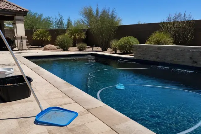 A technician cleaning a rectangular backyard pool in Phoenix, AZ with clear water and surrounding desert landscaping.
