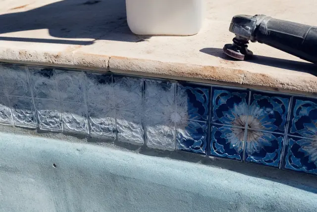 Close-up of mineral deposits being cleaned from pool tiles during an acid wash service in Phoenix, AZ.