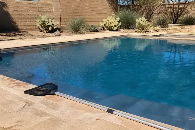 Telescopic pool net resting on a deck by a clear swimming pool with desert landscaping in Scottsdale, AZ.