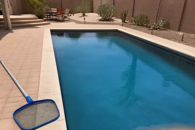 Clean residential swimming pool with a skimmer pole on a paver deck in Gilbert, AZ.