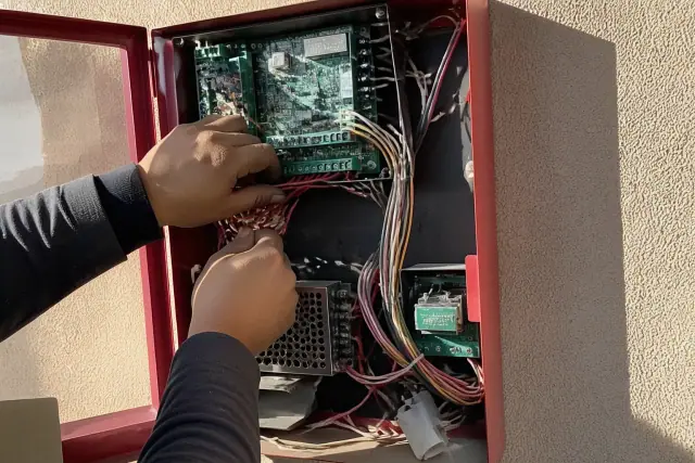 Technician wiring a fire alarm control panel on a stucco wall at a job site in Phoenix, AZ.