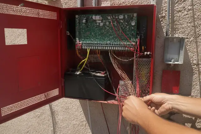 Technician wiring a fire alarm control panel cabinet on a stucco wall in Phoenix, AZ.