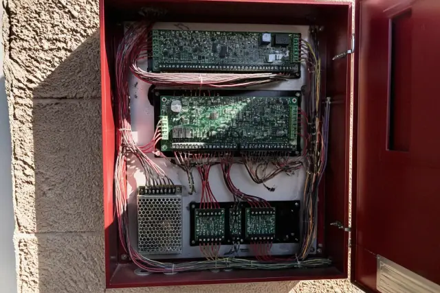 Interior of a wall-mounted fire alarm control panel with logic boards and cabling in Phoenix, AZ.