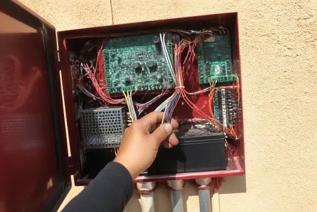 Technician wiring a fire alarm control panel cabinet on a stucco wall in Phoenix, AZ.