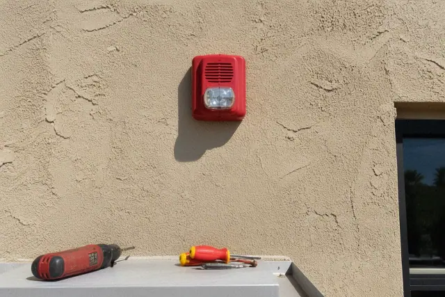 Wall-mounted fire alarm horn-strobe device installed on a stucco exterior wall in Phoenix, AZ.