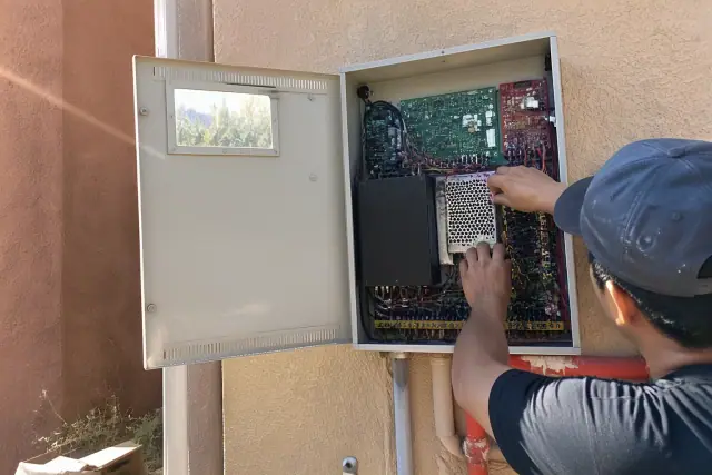 Technician wiring a fire alarm control panel cabinet on a stucco wall in Phoenix, AZ.