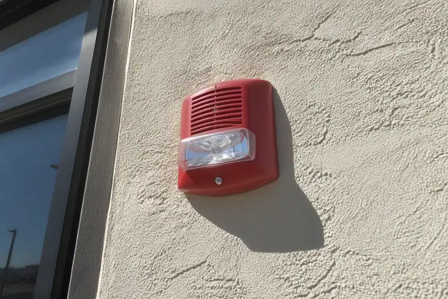 Wall-mounted horn-strobe fire alarm notification device on a stucco wall in Phoenix, AZ.