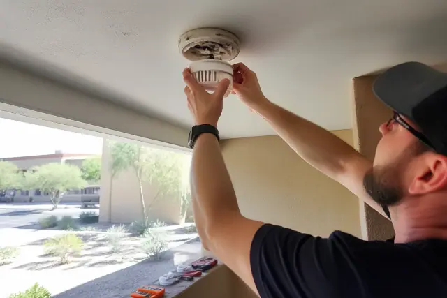 Technician installing a smoke detector on a commercial ceiling in Phoenix, AZ.