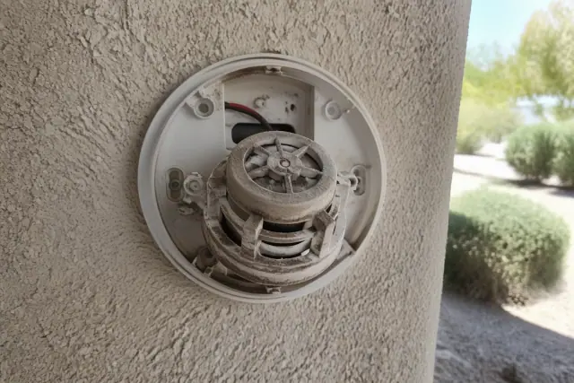 Close-up of dust buildup inside an open smoke detector sensor chamber at a job site in Phoenix, AZ.