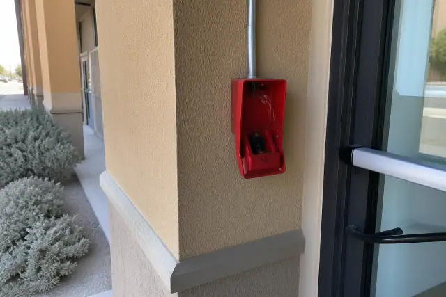 Red manual fire alarm pull station with exposed wiring on a stucco wall at a job site in Surprise, AZ.