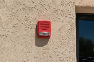 Wall-mounted horn-strobe notification device on a textured stucco exterior wall in Phoenix, AZ.