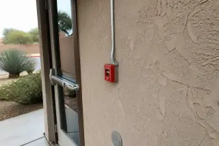 Red manual fire alarm pull station mounted on a stucco wall at a worksite in Phoenix, AZ.
