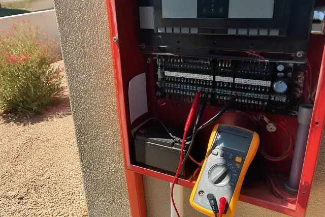 Technician using a multimeter to test a fire alarm terminal block at a building in Goodyear, AZ.