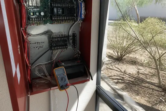 Multimeter testing fire alarm system terminal block wiring during maintenance in Glendale, AZ.