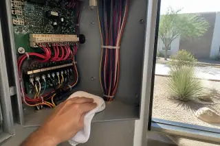 Technician cleaning the interior of a fire alarm control panel cabinet at a Phoenix, AZ worksite.