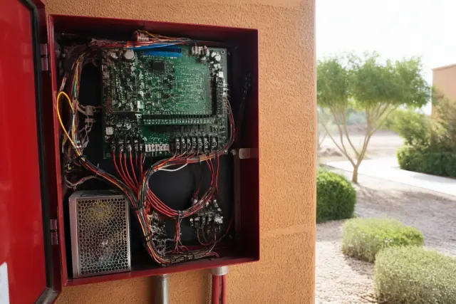 Technician hands wiring a fire alarm control panel cabinet with circuit boards in Goodyear, AZ.