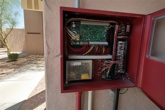 Technician hands wiring a fire alarm control panel on a stucco wall in Glendale, AZ.