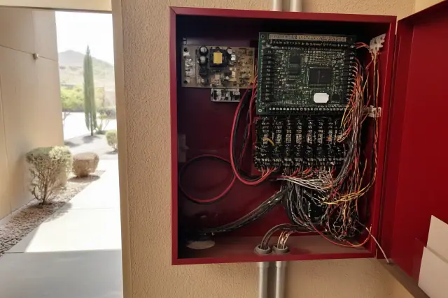 Technician wiring a fire alarm control panel with multicolored circuits in a Chandler, AZ building.