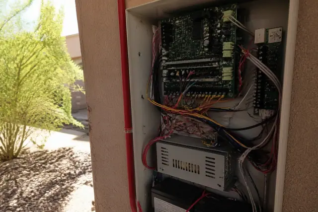 Technician wiring a fire alarm control panel cabinet on a stucco wall at a job site in Glendale, AZ.