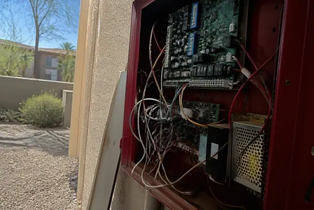 Technician repairing fire alarm system wiring inside a control panel in Tempe, AZ.