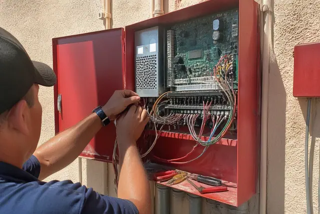 Technician repairing fire alarm control panel wiring on a stucco wall in Phoenix, AZ.