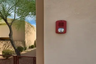 White horn-strobe notification device mounted on a stucco wall at a Phoenix, AZ worksite.