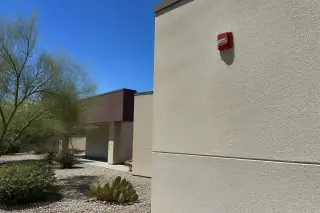 Wall-mounted fire alarm horn-strobe beside a desert landscape at a Phoenix, AZ construction site.
