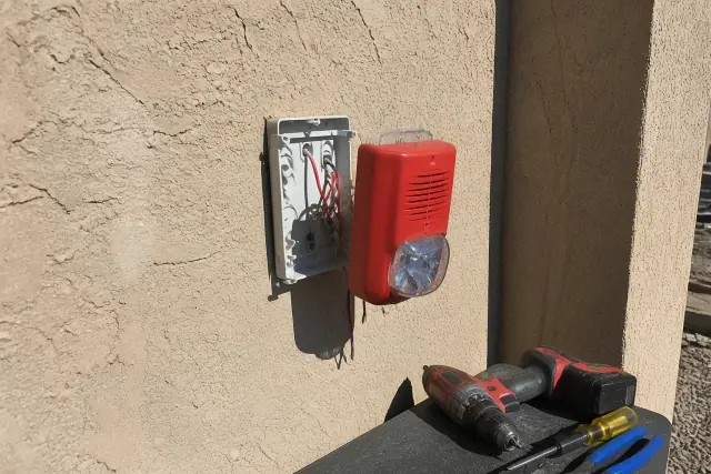 Technician installing a fire alarm horn-strobe device on a stucco wall at a worksite in Phoenix, AZ.
