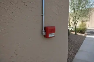 Wall-mounted fire alarm notification device on a sunny stucco wall at a construction site in Phoenix, AZ.