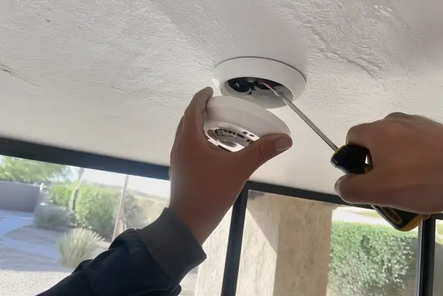 Technician installing a smoke detector on a commercial ceiling in Chandler, AZ.