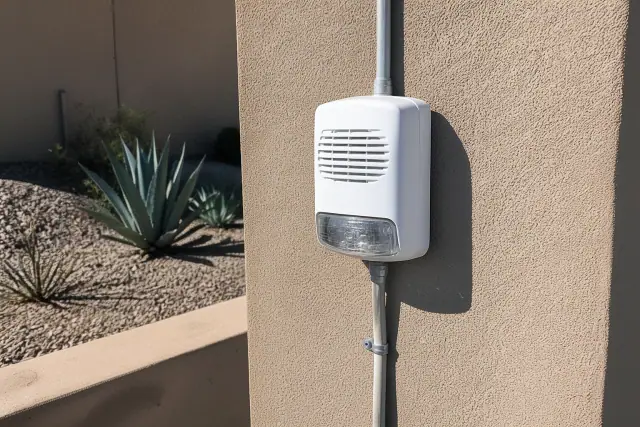 Fire alarm horn-strobe device mounted on a tan stucco wall in Gilbert, AZ.