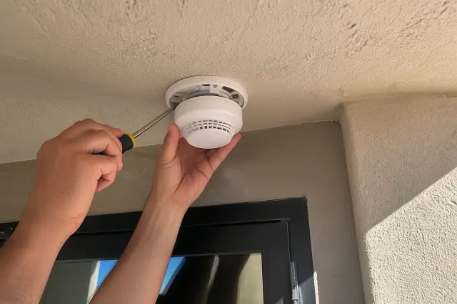 Technician installing a smoke detector on a commercial ceiling in Mesa, AZ.