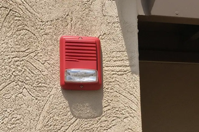 Fire alarm horn-strobe device being installed on a stucco wall at a residential property in Surprise, AZ.