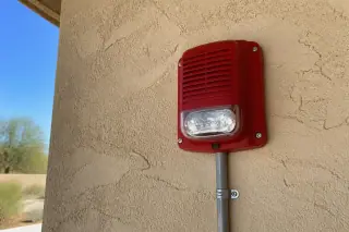 Fire alarm horn-strobe mounted on a textured stucco wall at a worksite in Phoenix, AZ.