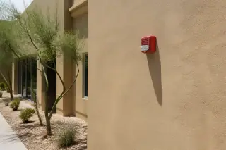 Fire alarm horn-strobe device installed on a stucco wall at a worksite in Phoenix, AZ.
