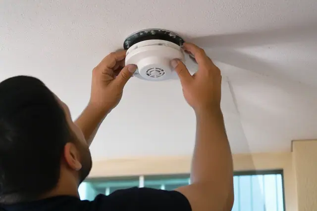 Technician installing a smoke detector on a commercial ceiling in Avondale, AZ.