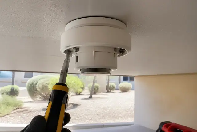 Technician installing a smoke detector on a ceiling junction box at a jobsite in Surprise, AZ.