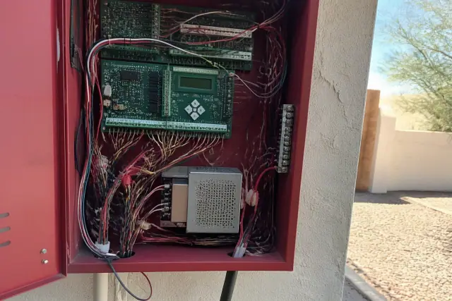 Hands wiring multicolored circuits inside a wall-mounted fire alarm control panel in Mesa, AZ.