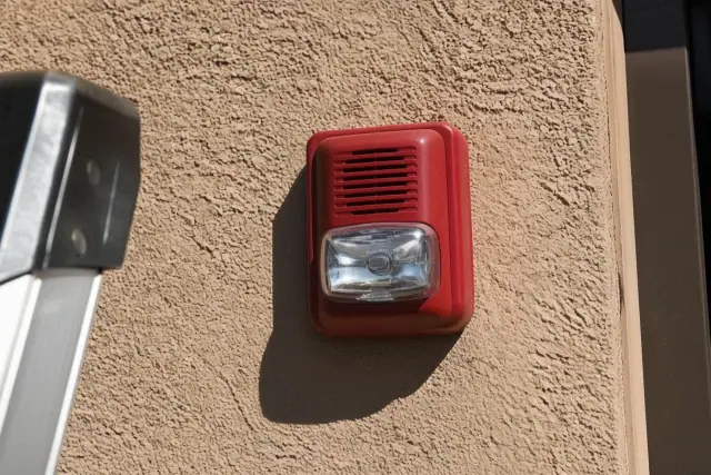 Wall-mounted horn-strobe fire alarm device installed on a stucco wall at a jobsite in Tempe, AZ.